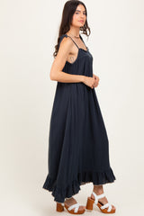 woman wearing a navy blue sleeveless maxi dress with ruffle hem and tie straps, paired with white platform sandals