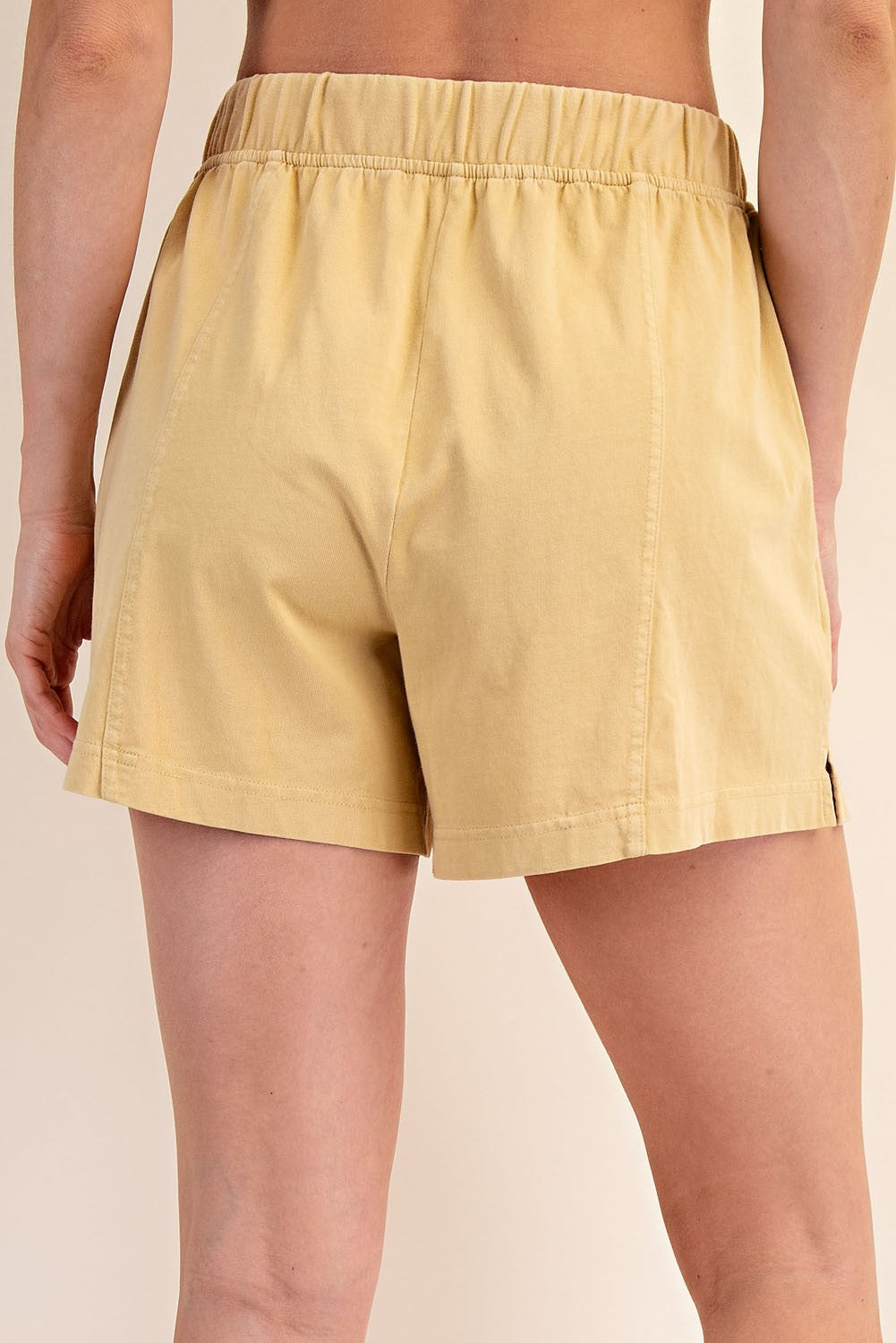 woman wearing yellow high-waisted shorts, showing the back view with elastic waistband and relaxed fit