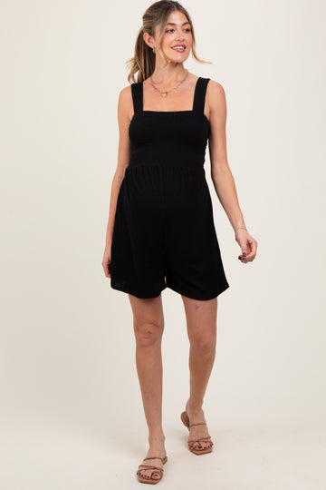 woman wearing a black maternity romper with a smocked bodice and wide straps, showcasing her baby bump