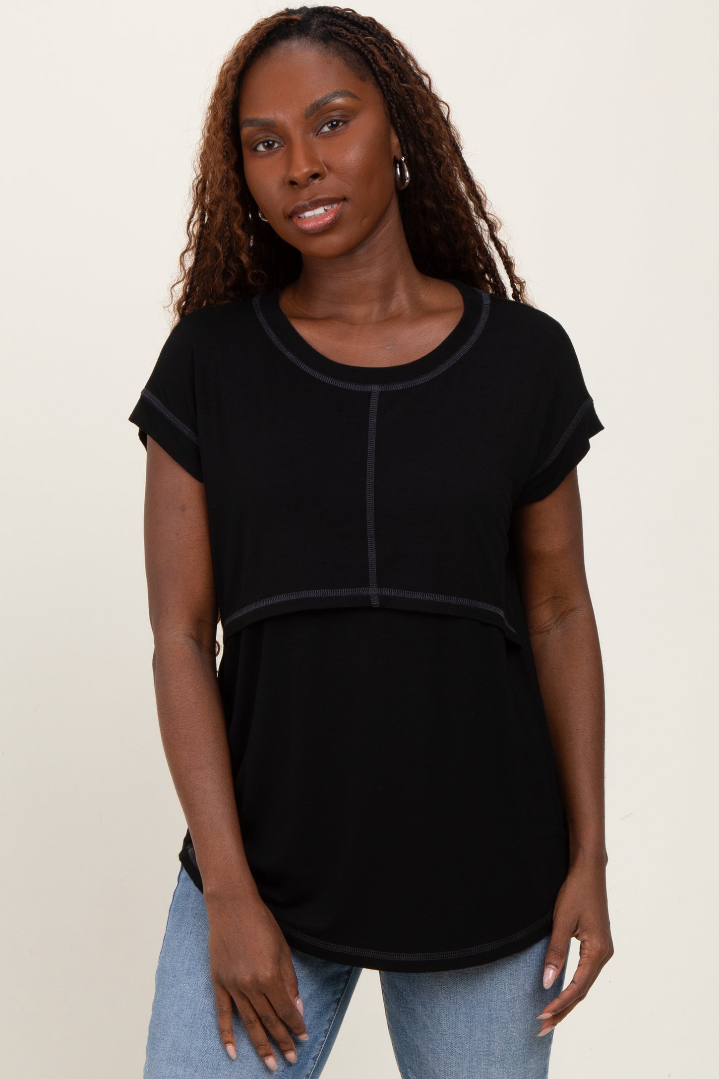 woman wearing a black short sleeve top with a layered design and round neckline, styled with light blue jeans