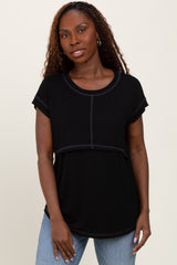 woman wearing a black short sleeve top with a layered design and round neckline, styled with light blue jeans