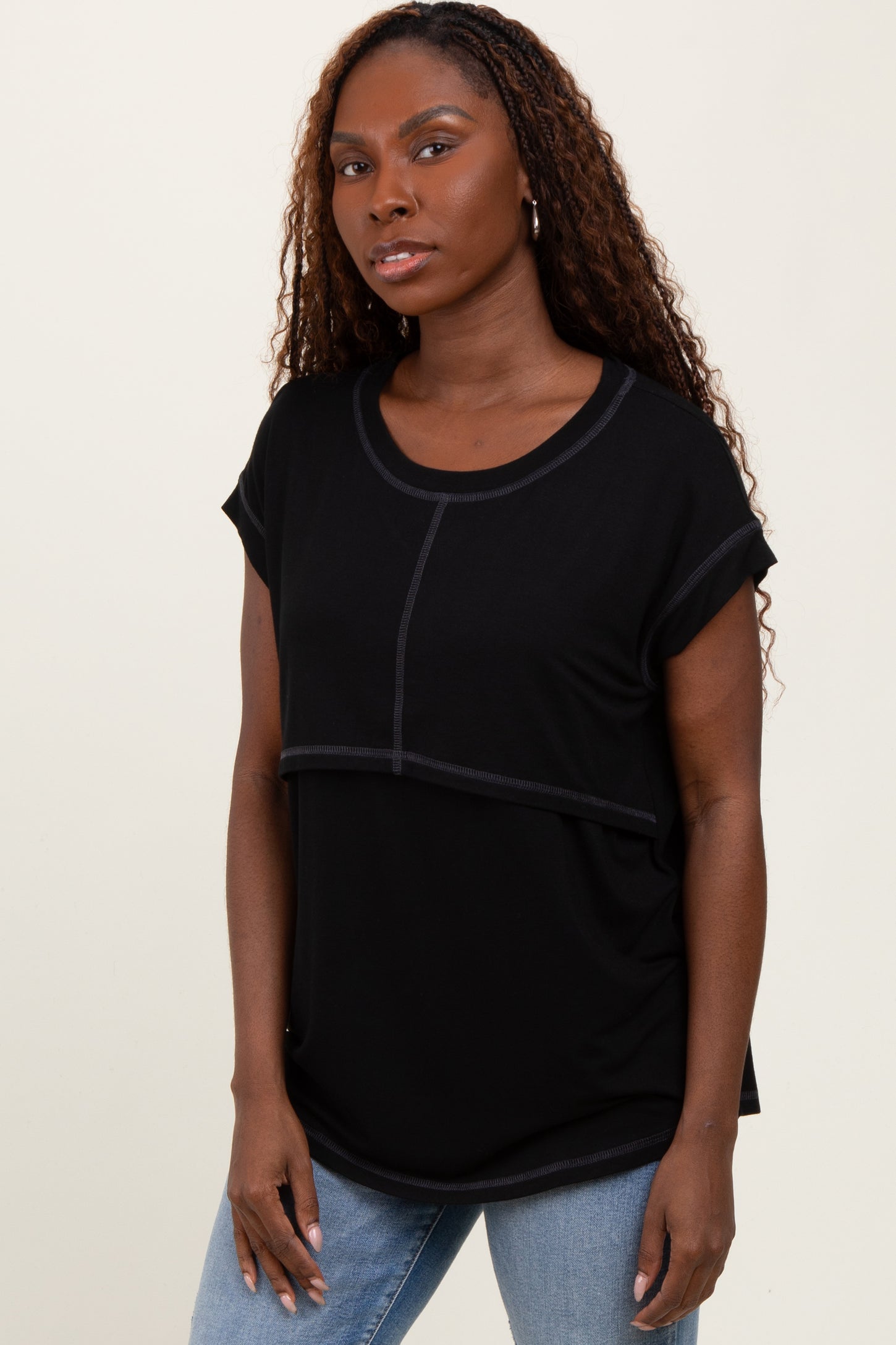 woman wearing a black short sleeve top with a scooped neckline and contrast stitching, paired with light blue jeans