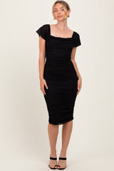 woman wearing a black fitted dress with ruched detailing and short sleeves, posing against a plain background