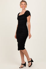woman wearing a black ruched bodycon dress with short cap sleeves and a square neckline, standing with a smile