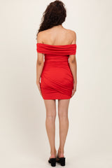 woman wearing a fitted red off-shoulder dress with ruched detailing, styled with open-toe heels, showing the back view