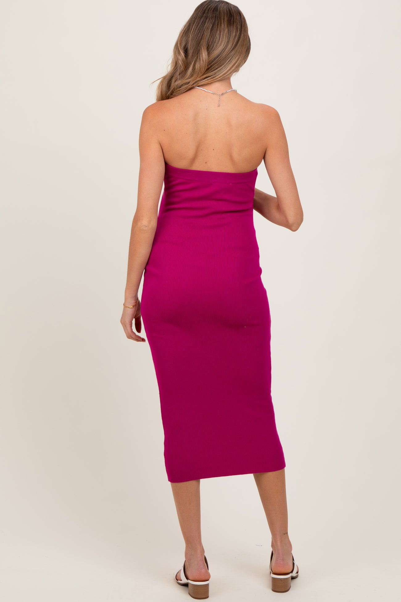 woman wearing a bright pink strapless maternity dress with a fitted silhouette and midi length from the back