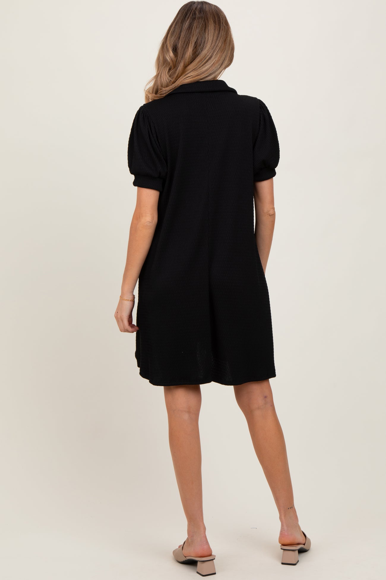 woman wearing a black maternity dress with puff sleeves, showing a relaxed fit from the back