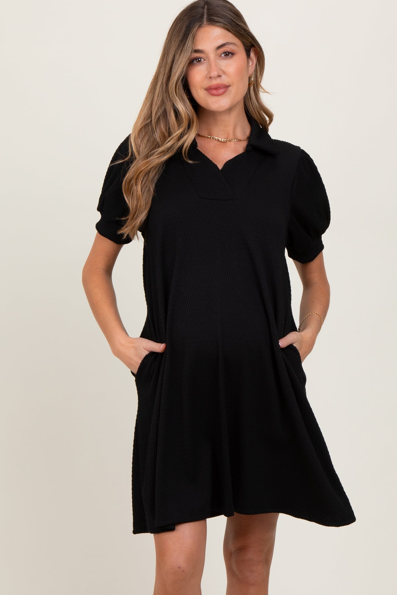 woman wearing a black short sleeve maternity dress with a collar and side pockets, showing a baby bump