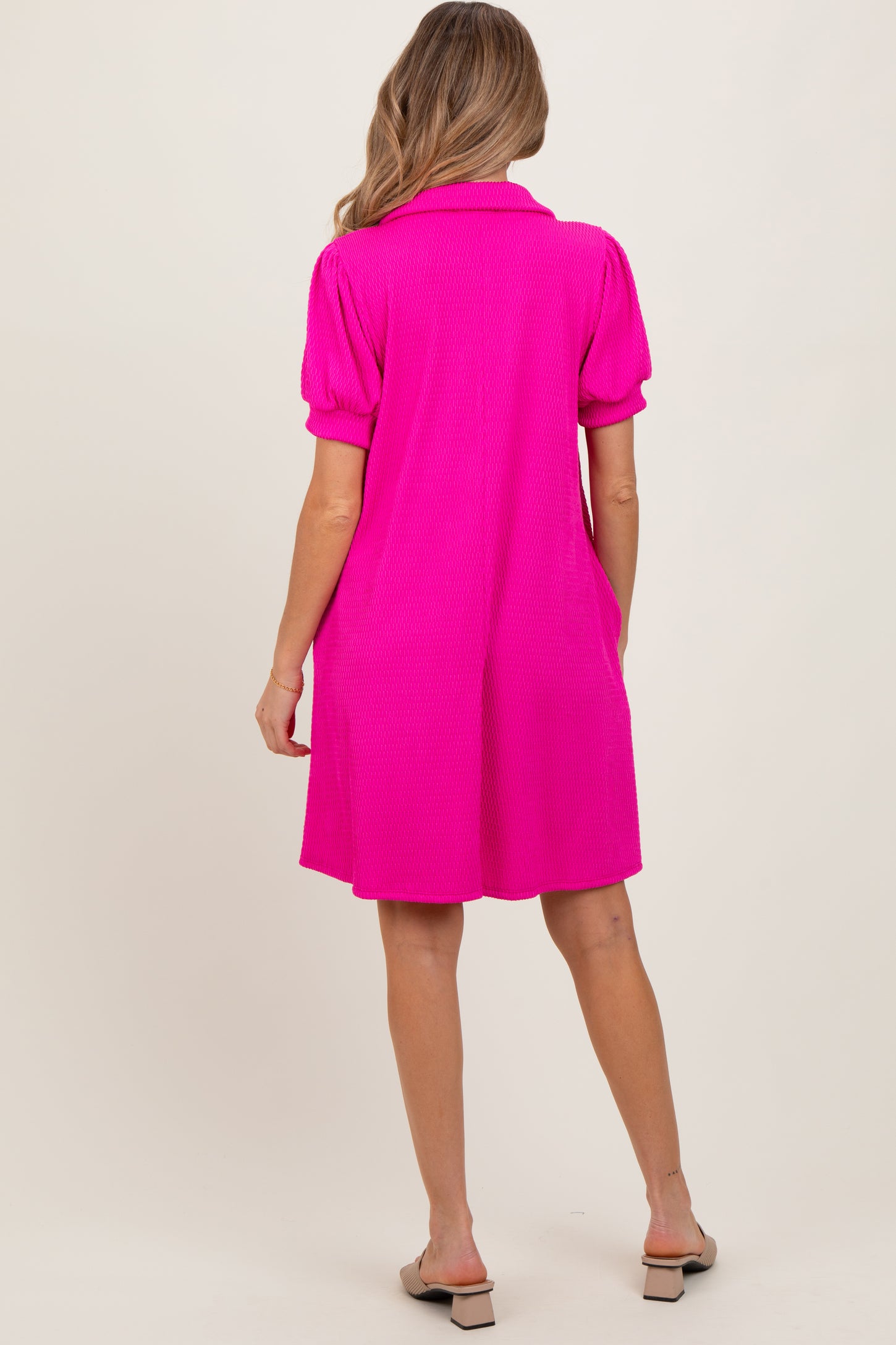 woman wearing a bright pink short sleeve maternity dress with a collar, shown from the back