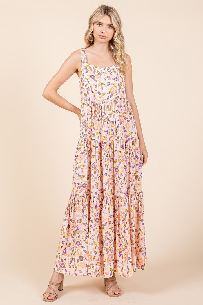 woman wearing a floral print maxi dress in pink and yellow with tiered details and spaghetti straps
