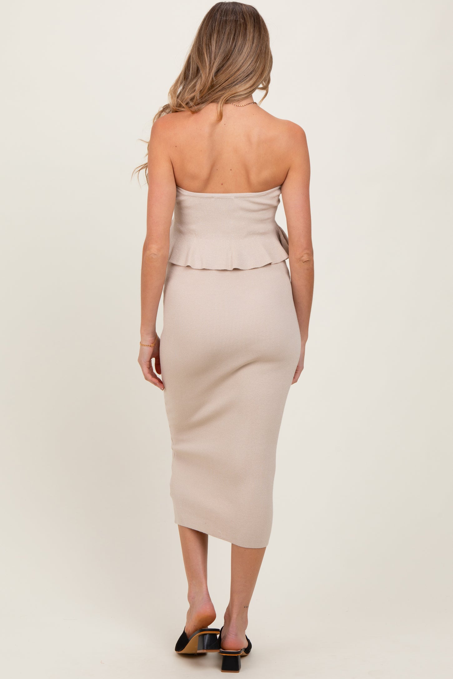 woman wearing a beige strapless ribbed maternity dress with a ruffled hem and mid-length fit