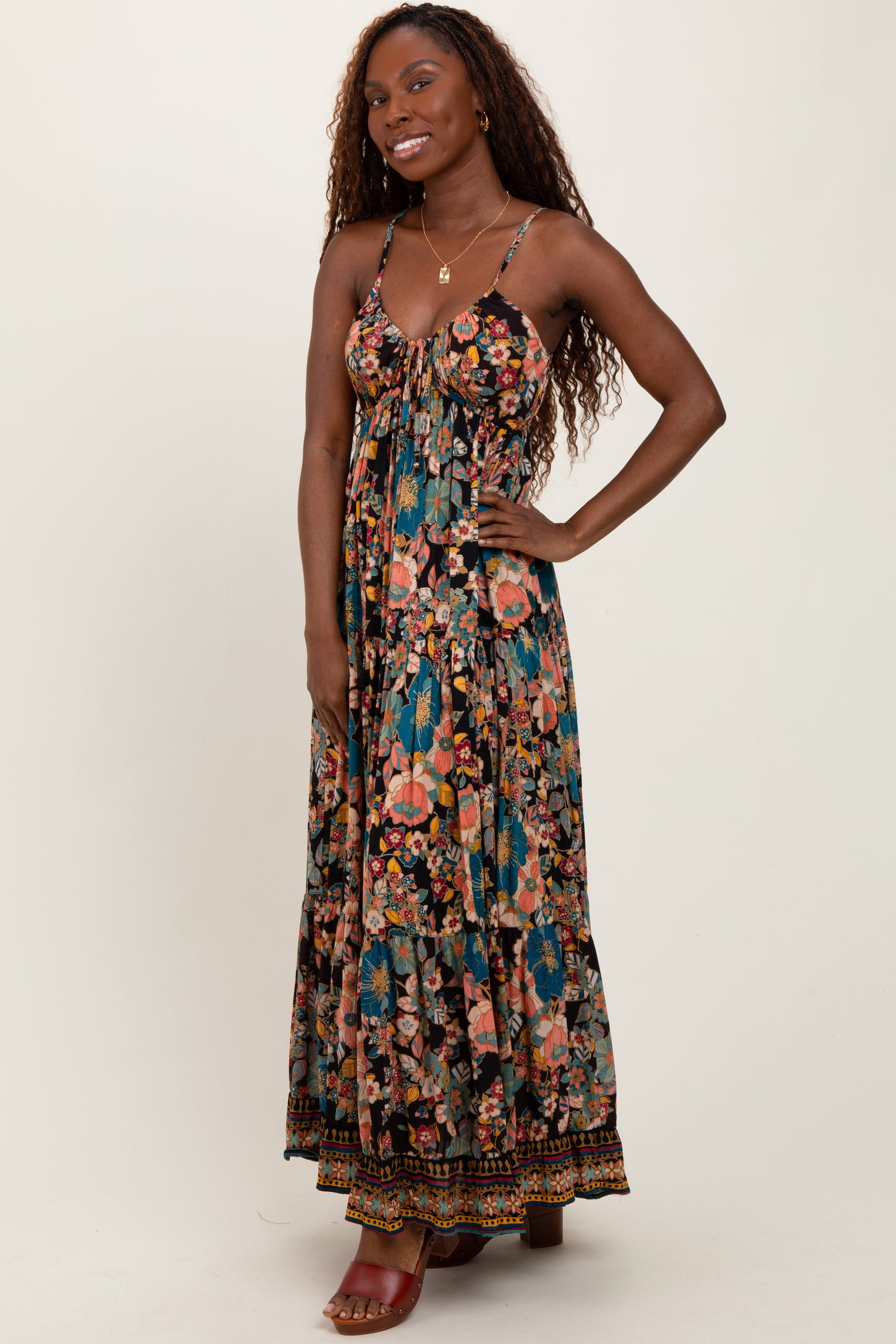 woman wearing a black floral maxi dress with a flowy silhouette and spaghetti straps, smiling with hands on hips