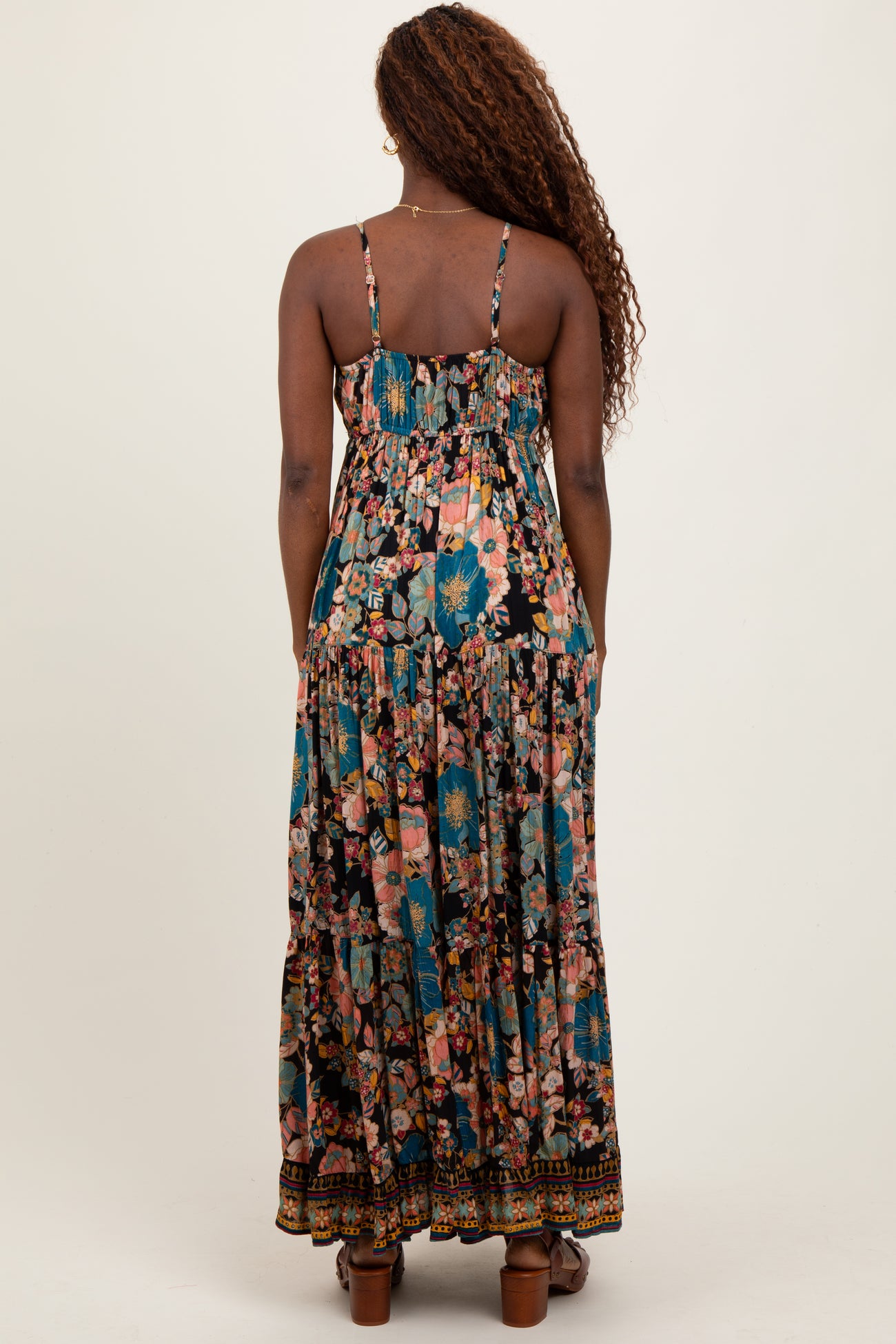woman wearing a black floral maxi dress with spaghetti straps and tiered detailing, viewed from the back