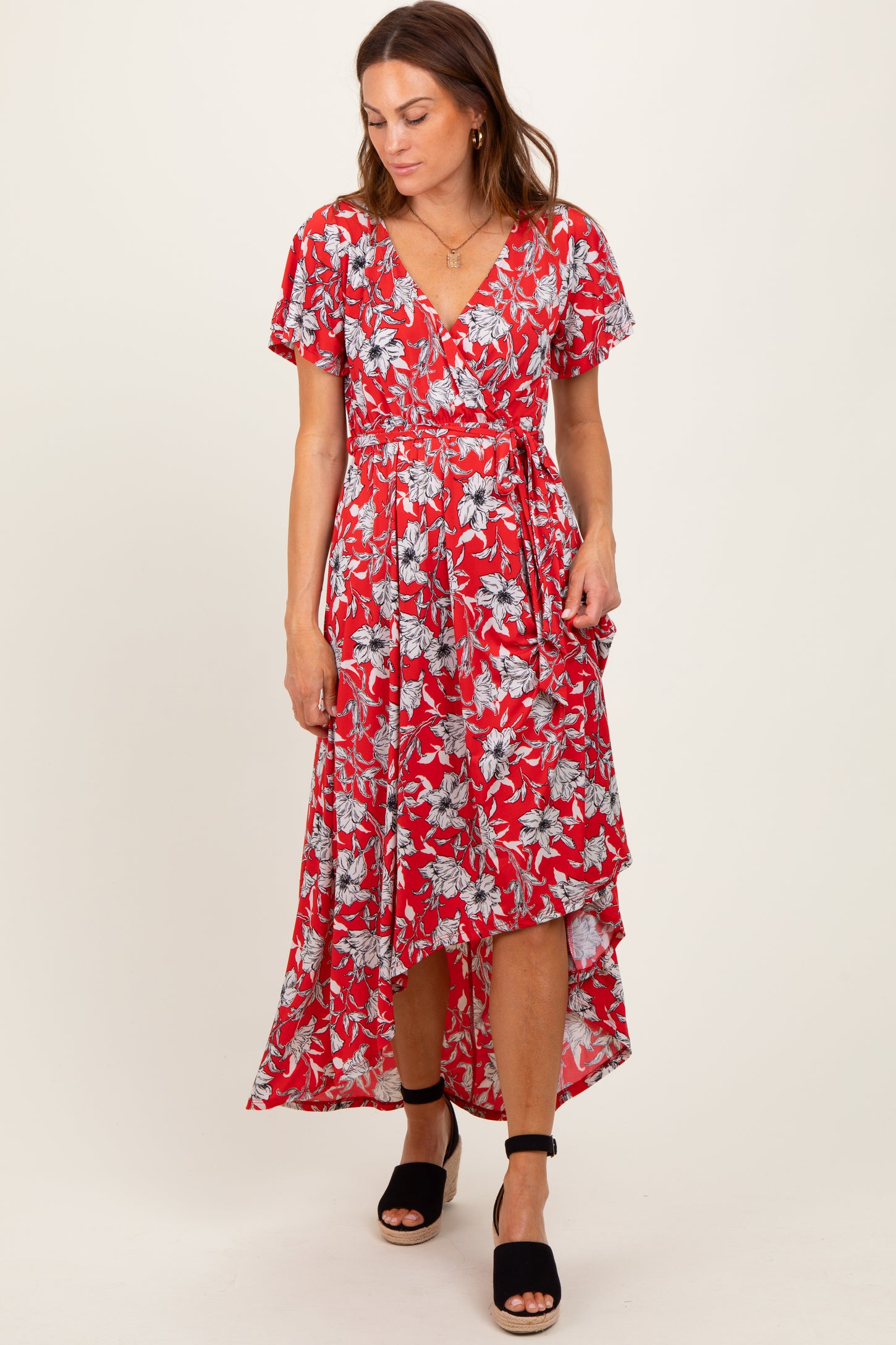 woman wearing a red floral wrap dress with short sleeves and a high-low hemline, styled with black heeled sandals