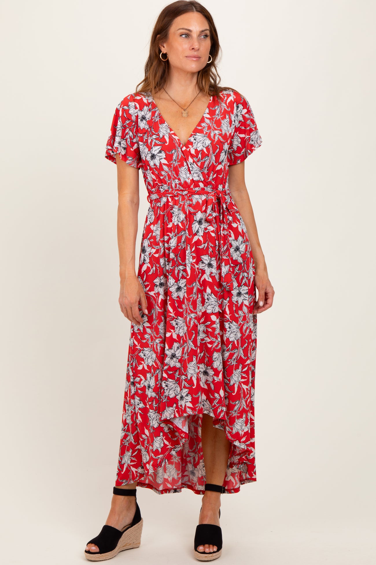 woman wearing a red floral maxi dress with short sleeves and a high-low hemline, standing in a relaxed pose