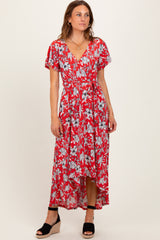 woman wearing a red floral maxi dress with short sleeves and a high-low hemline, standing in a relaxed pose