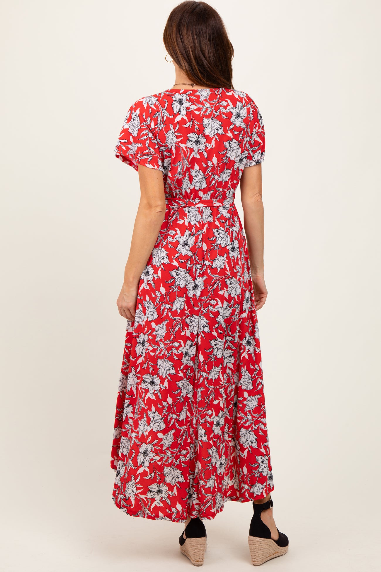 woman wearing a red floral maxi dress with short sleeves and a tie waist, viewed from the back