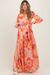 woman wearing a pink floral maternity maxi dress with long sleeves and a waist tie, holding her baby bump