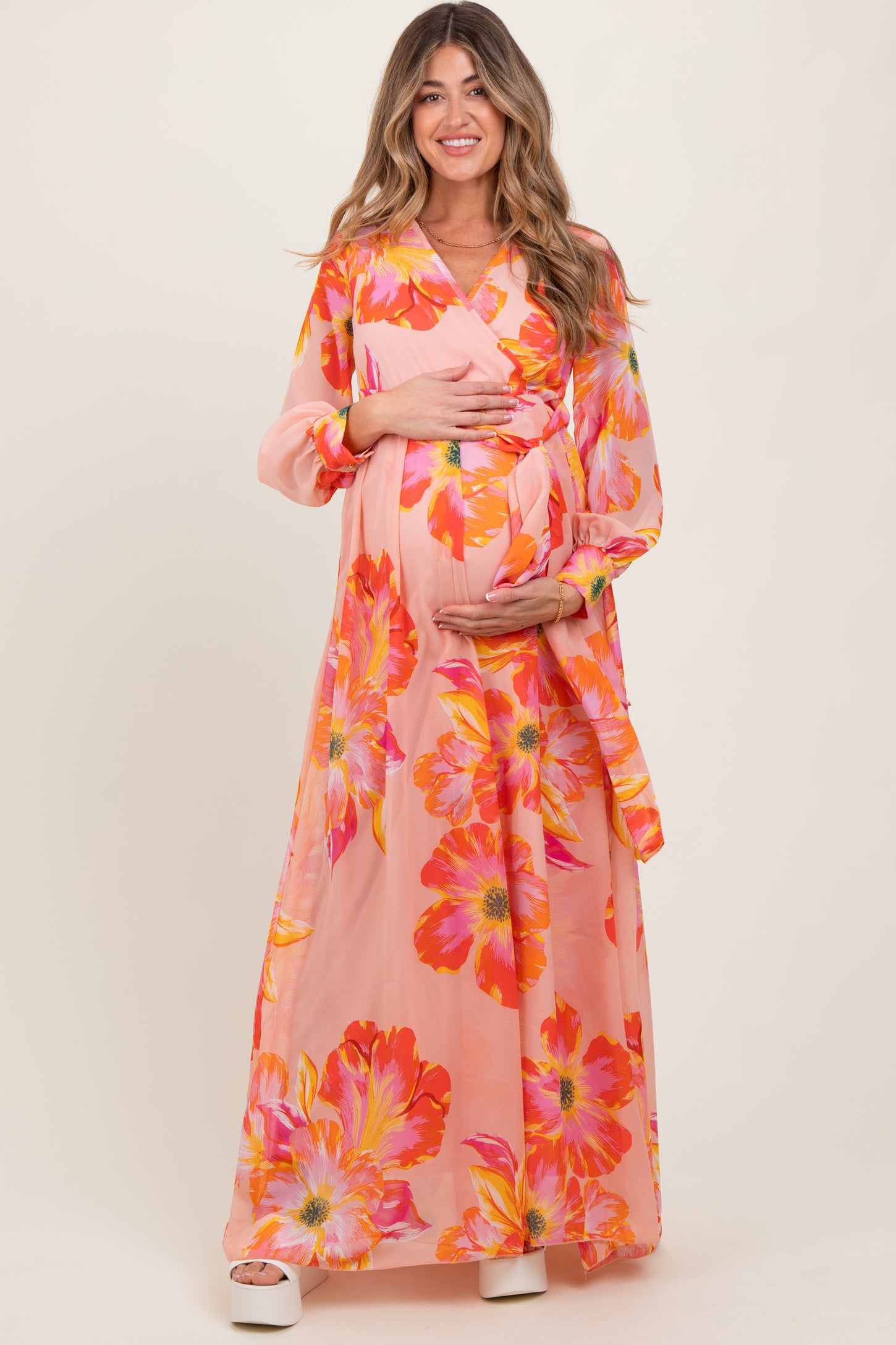 woman wearing a pink floral maternity maxi dress and holding her baby bump