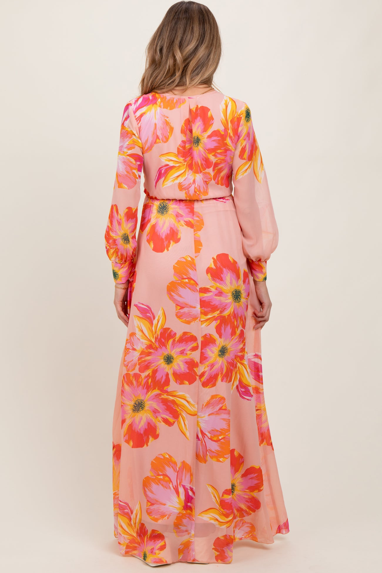woman wearing a long pink floral maternity maxi dress with long sleeves, showing a flowy back design