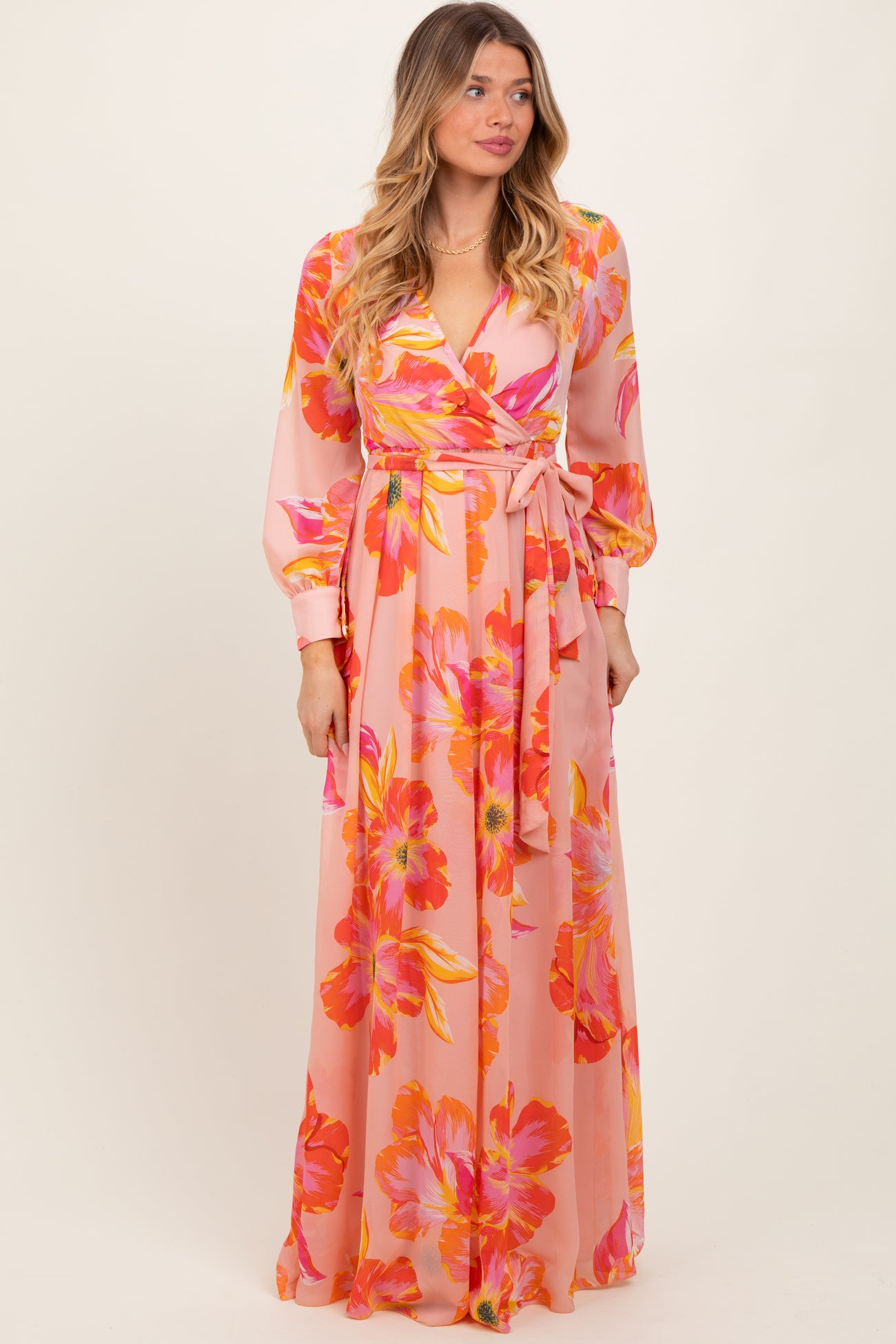 woman wearing a pink floral maxi dress with long sleeves and a wrap tie detail