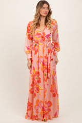 woman wearing a pink floral maxi dress with long sleeves and a wrap tie detail