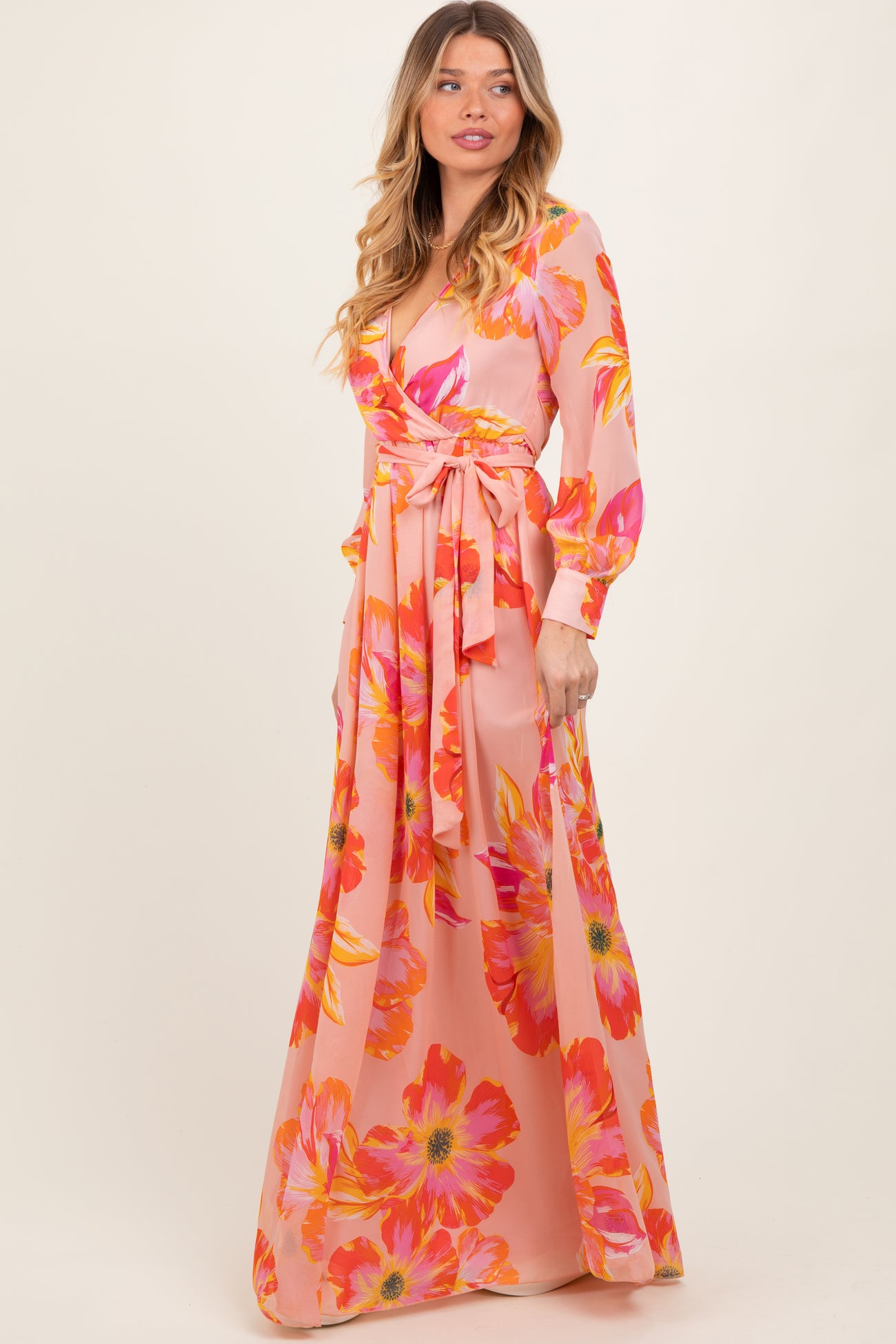 woman wearing a pink floral maxi dress with long sleeves and a tie waist detail