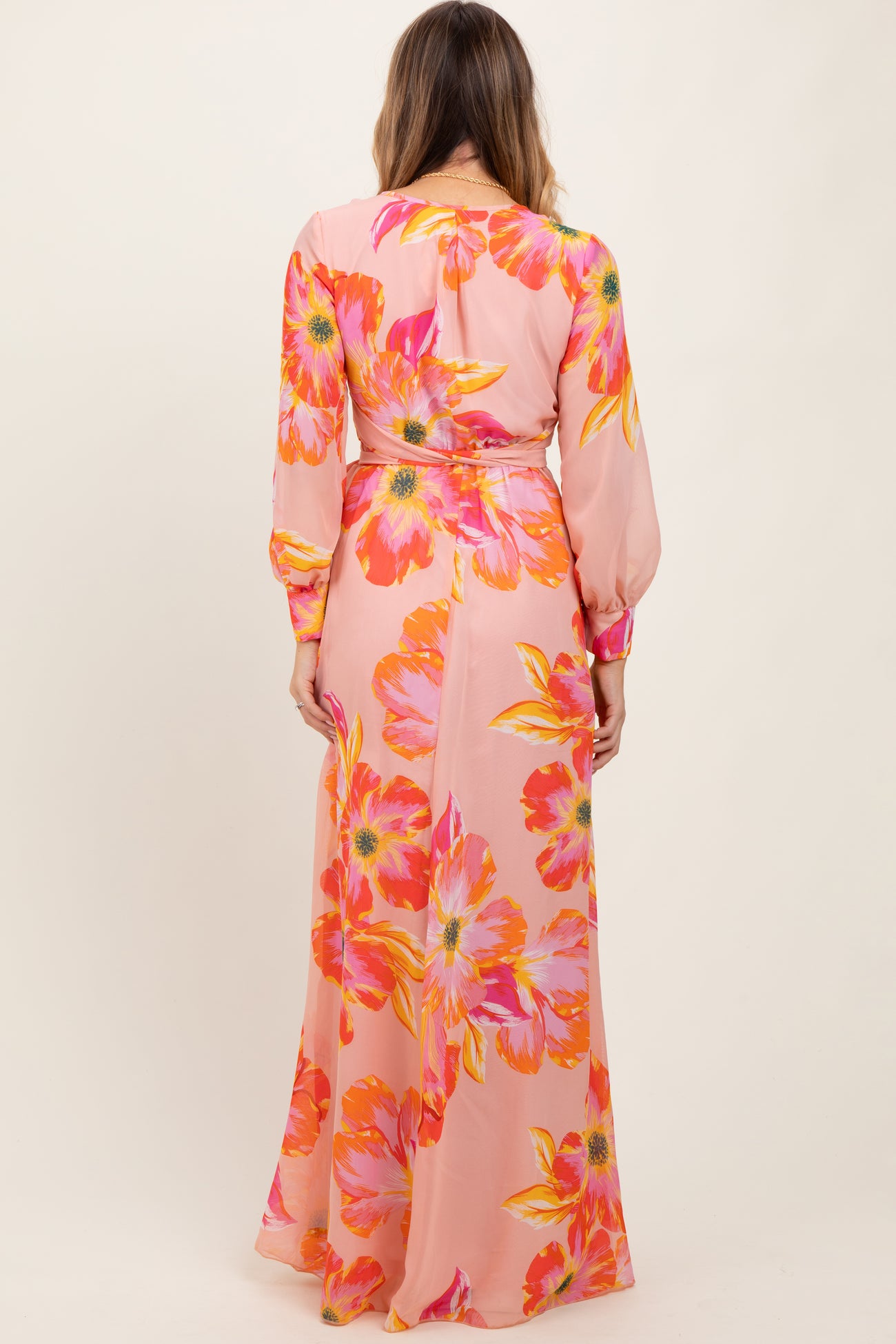 woman wearing a pink floral maxi dress with long sleeves and a cinched waist seen from the back