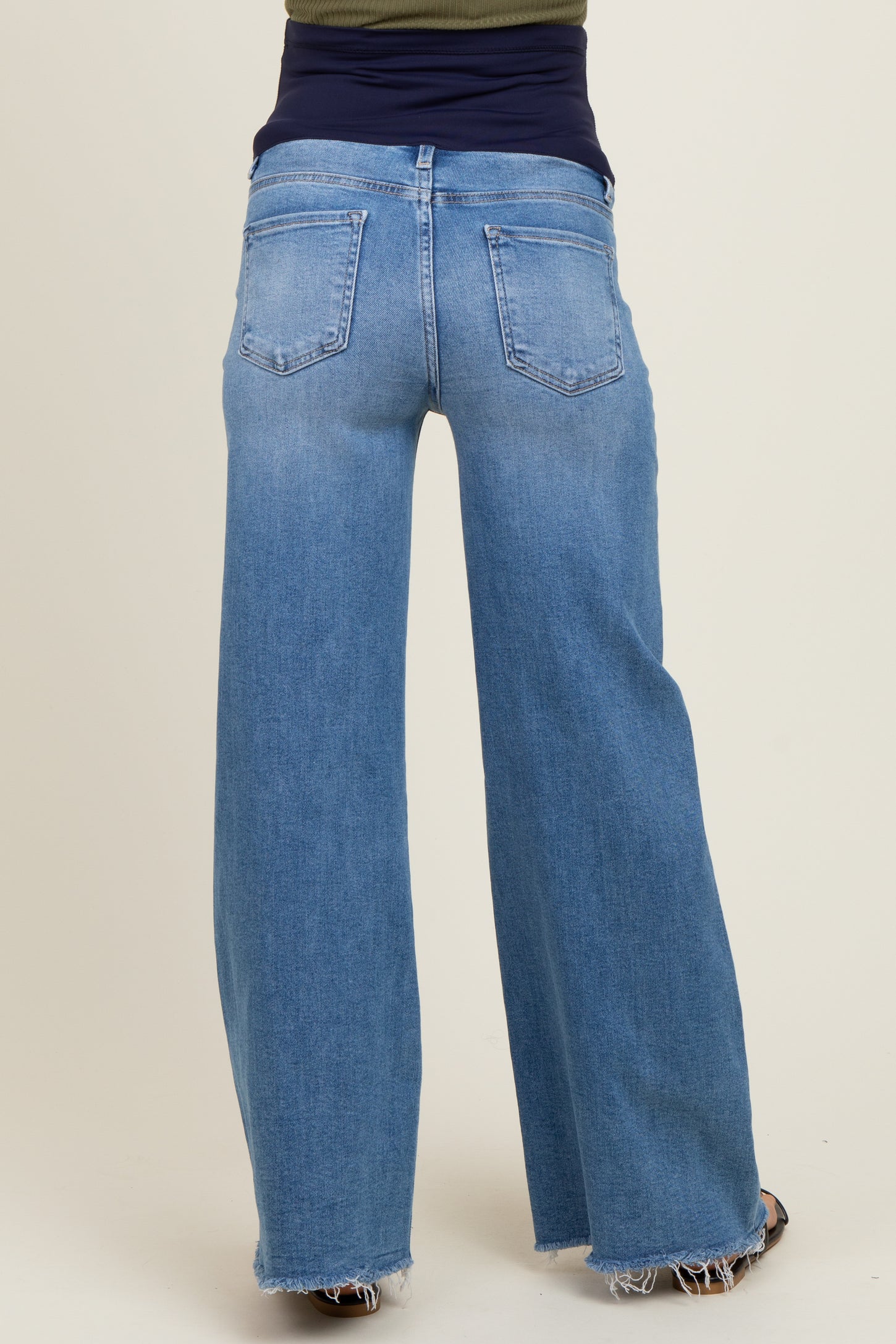 maternity wear light blue wide leg jeans with a distressed hem, styled with a navy maternity top, view from the back