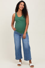 woman wearing a green maternity tank top and blue wide-leg jeans, showing her baby bump