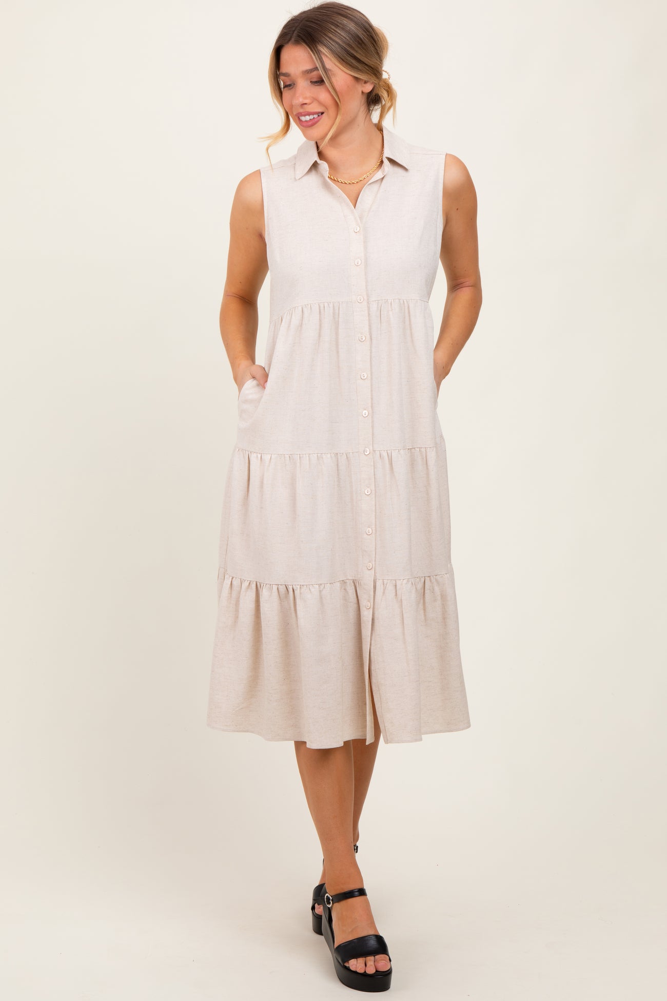 woman wearing a beige sleeveless button-up tiered midi dress with side pockets and black platform heels