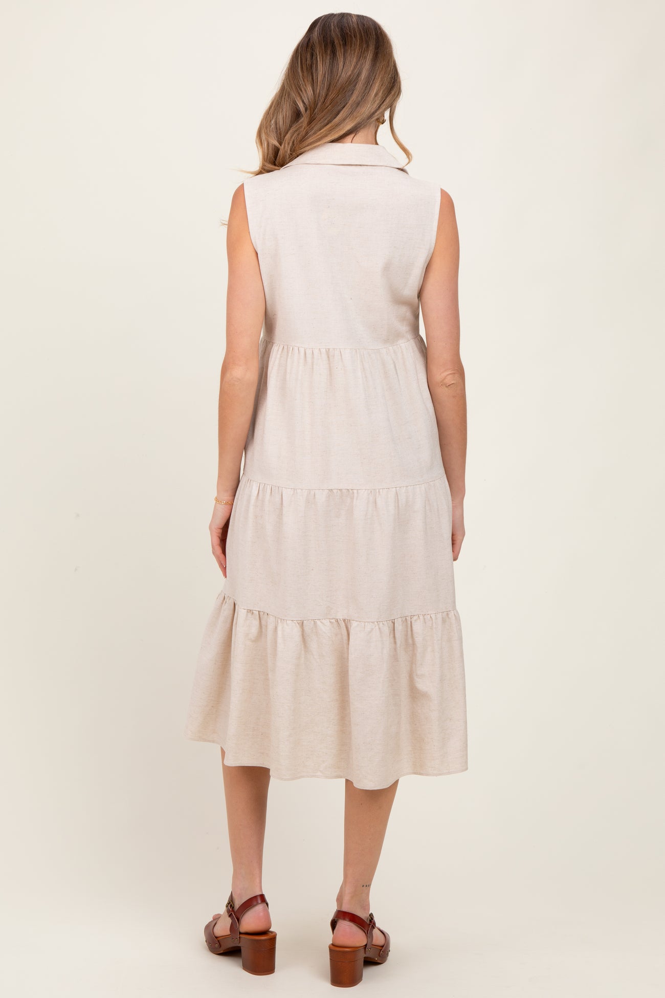 woman wearing a light beige sleeveless maternity dress with a tiered skirt and back button details