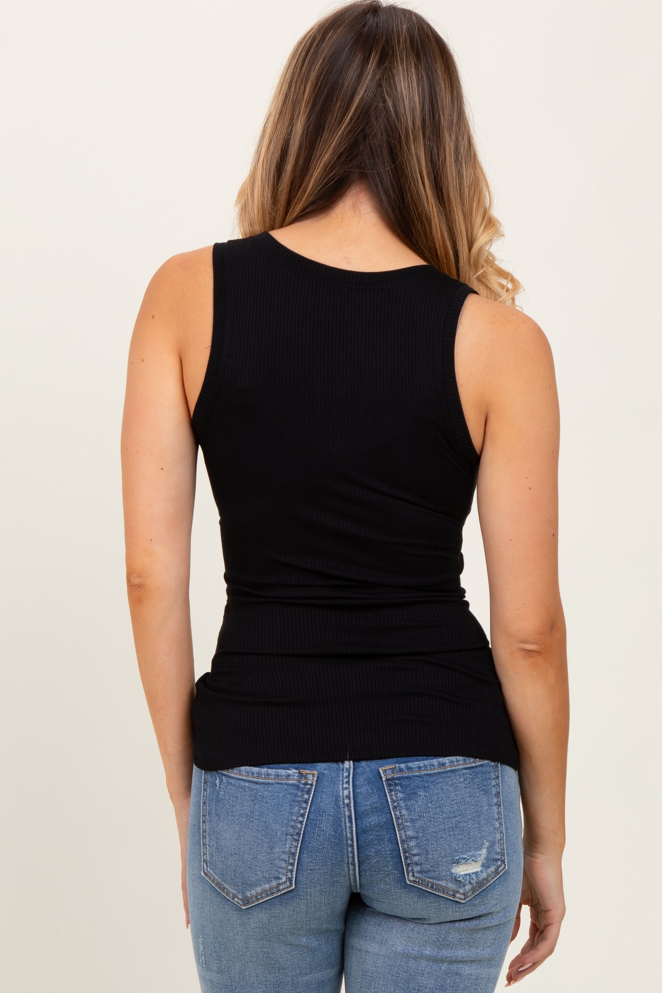 woman wearing a fitted black ribbed tank top and light blue distressed jeans, viewed from the back