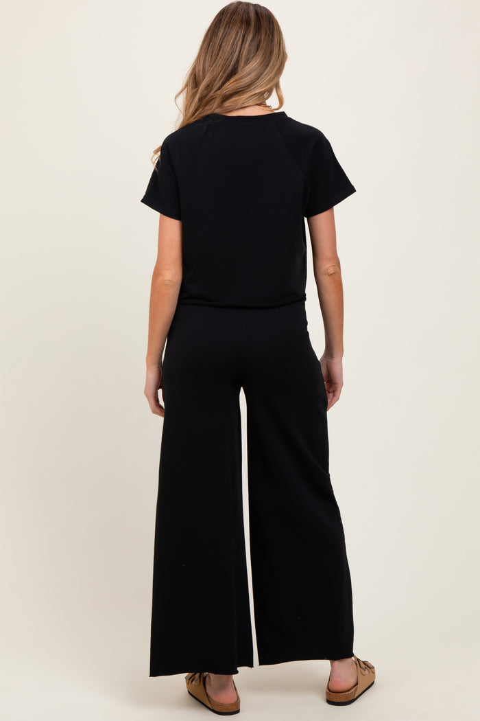 woman wearing a black short sleeve maternity jumpsuit with wide leg pants, showing the back view