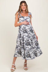 woman wearing a floral print maternity dress with shoulder ties, showcasing her baby bump, styled with wedge sandals