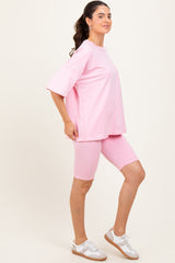 woman wearing a pink oversized t-shirt and matching pink bike shorts, posing with one hand on her hip