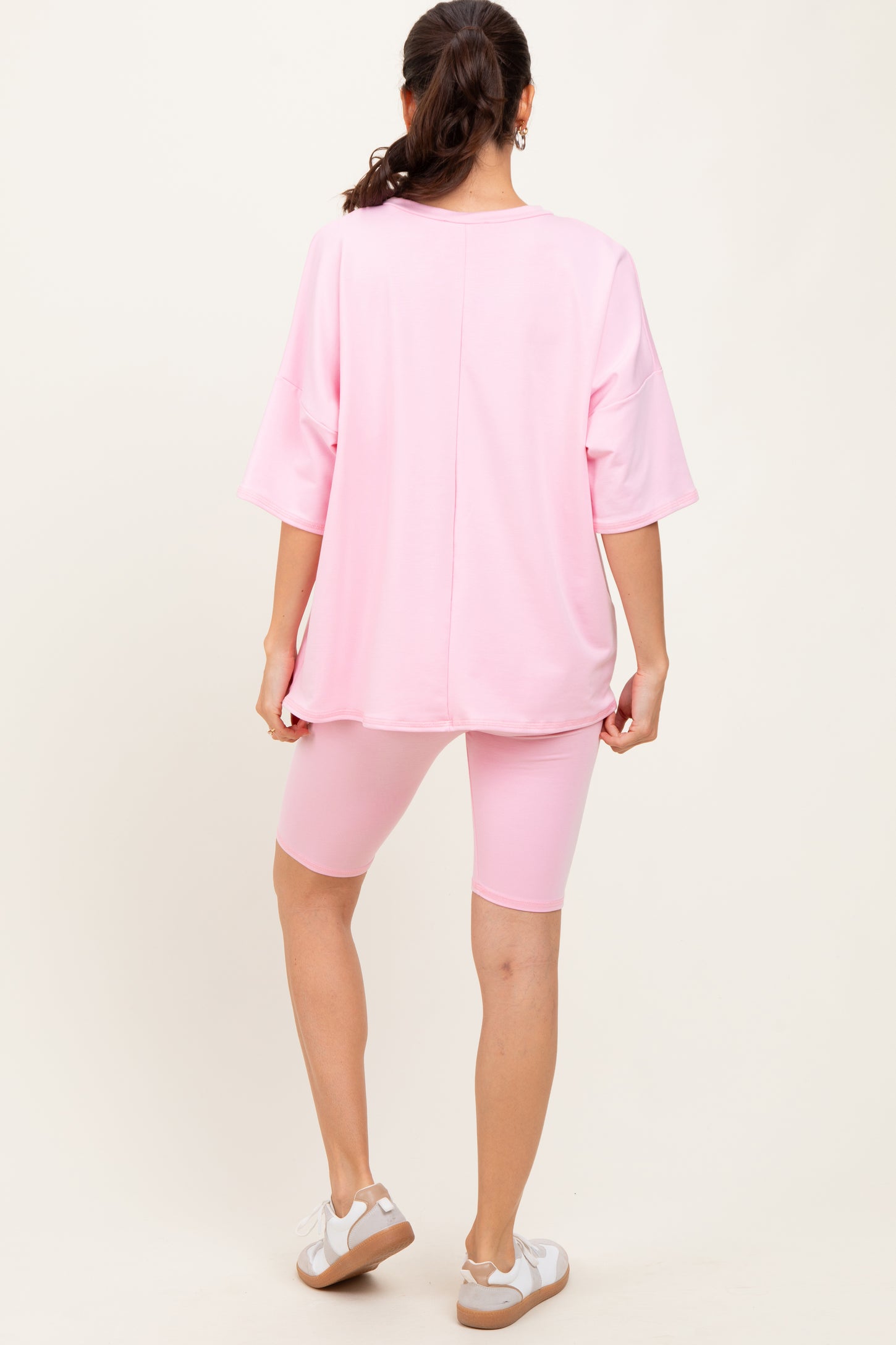 woman wearing a pink oversized t-shirt and matching bike shorts, standing with her back to the camera
