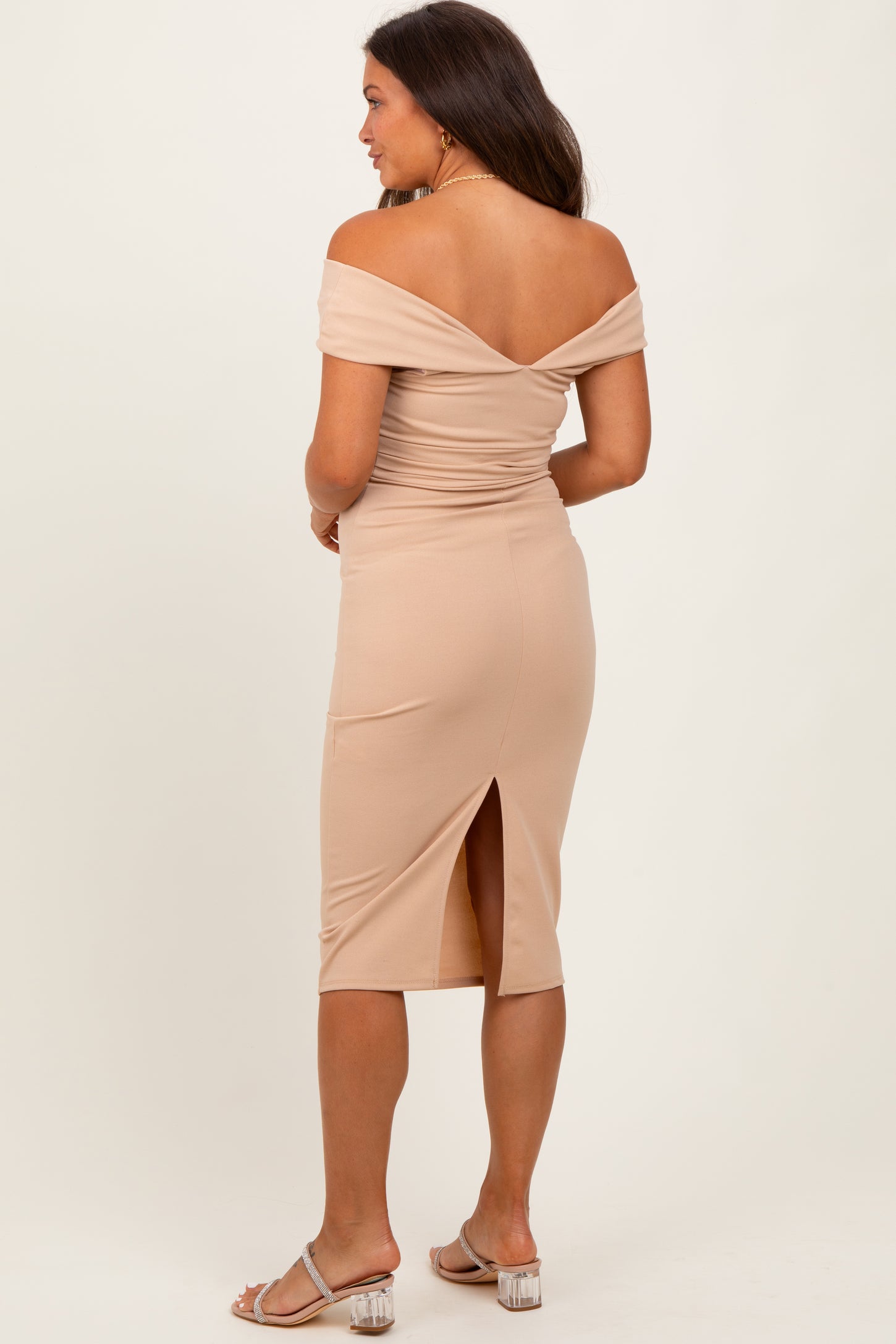 woman wearing a nude off-the-shoulder maternity dress with a side slit, showing a fitted silhouette from the back