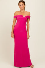 woman wearing a vibrant pink off-the-shoulder evening gown with ruched detailing and a gold emblem on the bust