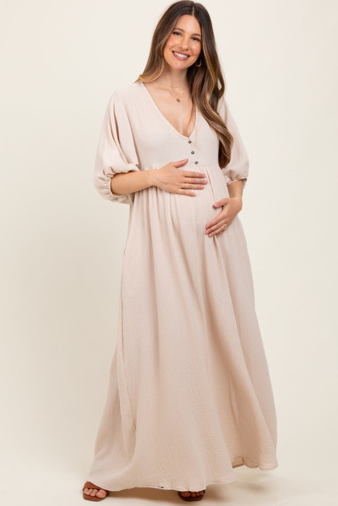 woman wearing a blush maternity maxi dress with button details, holding her baby bump