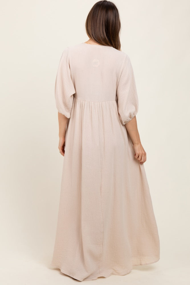 woman wearing a flowy light beige maternity dress with puff sleeves and a tiered design, showcasing a baby bump