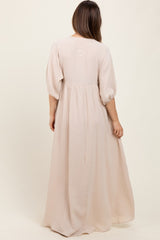 woman wearing a flowy light beige maternity dress with puff sleeves and a tiered design, showcasing a baby bump