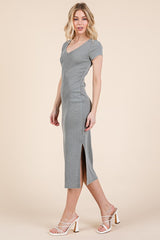 woman wearing a fitted gray midi dress with short sleeves and a side slit, paired with white heeled sandals