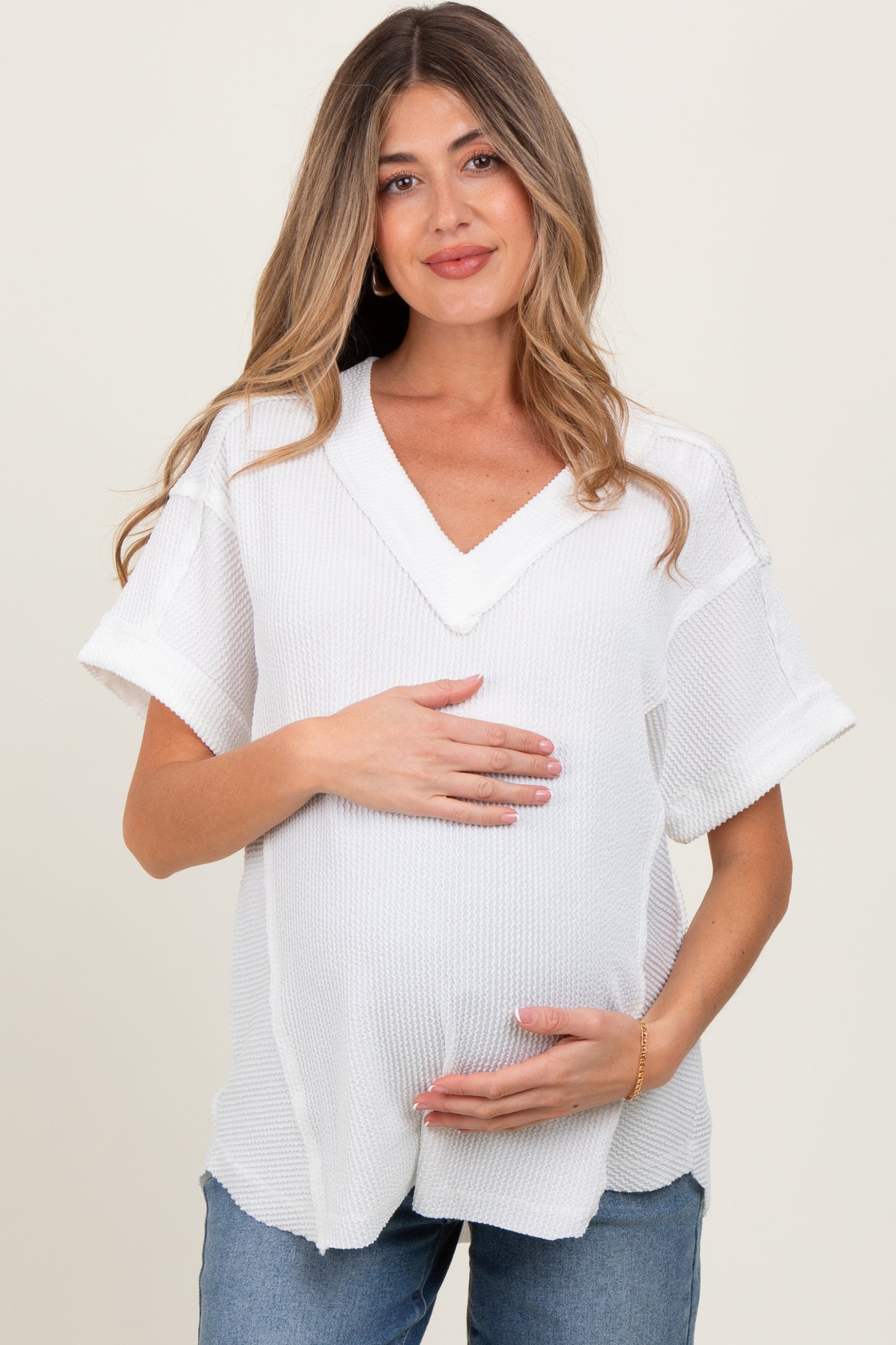 woman wearing a white short sleeve maternity top and holding her baby bump