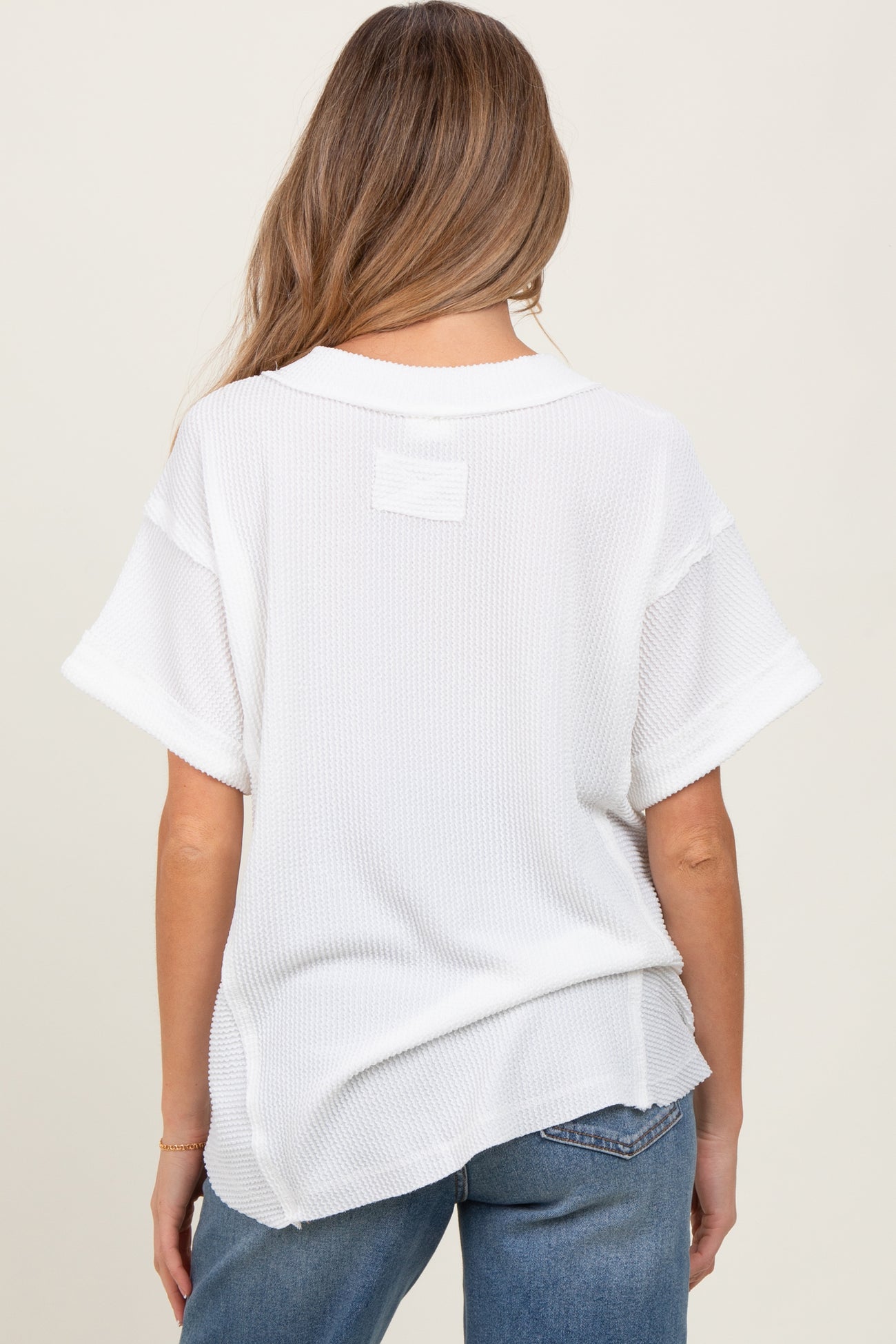 woman wearing a white short sleeve maternity top with a relaxed fit and a textured fabric, showing the back view