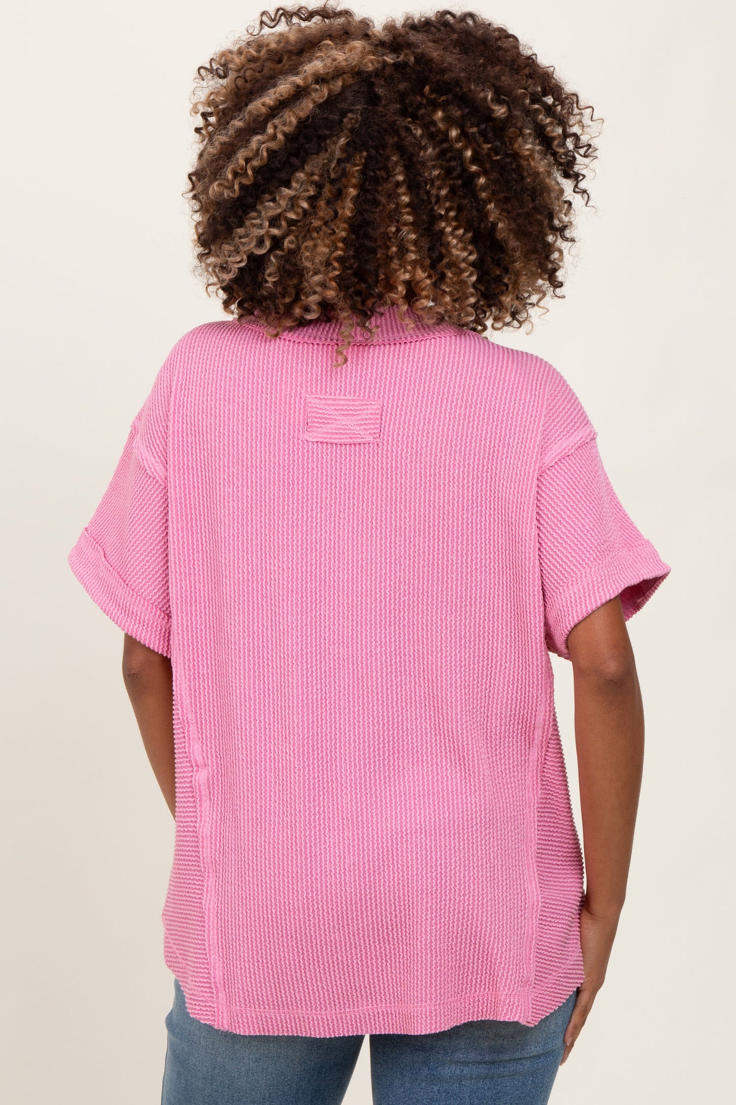woman wearing a pink oversized maternity top with short sleeves and a relaxed fit, seen from the back