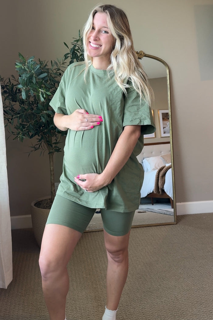 woman wearing an olive green short sleeve maternity t-shirt and matching bike shorts, holding her baby bump