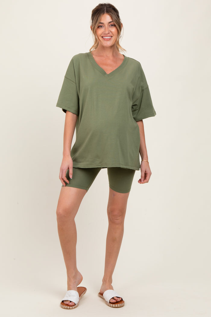 woman wearing an olive green oversized v-neck maternity tee and matching bike shorts, showing her baby bump
