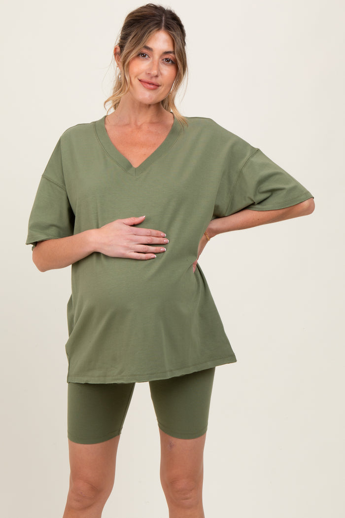 woman wearing a green oversized v-neck maternity t-shirt and matching bike shorts, holding her baby bump