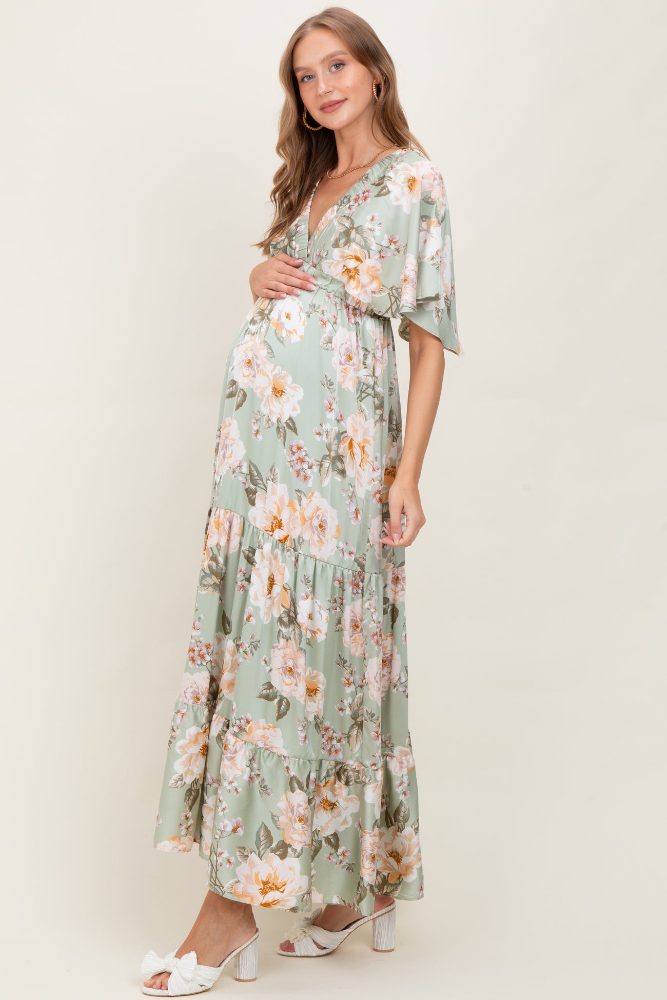 woman wearing a floral mint green maternity maxi dress with short sleeves and a v-neck, cradling her baby bump